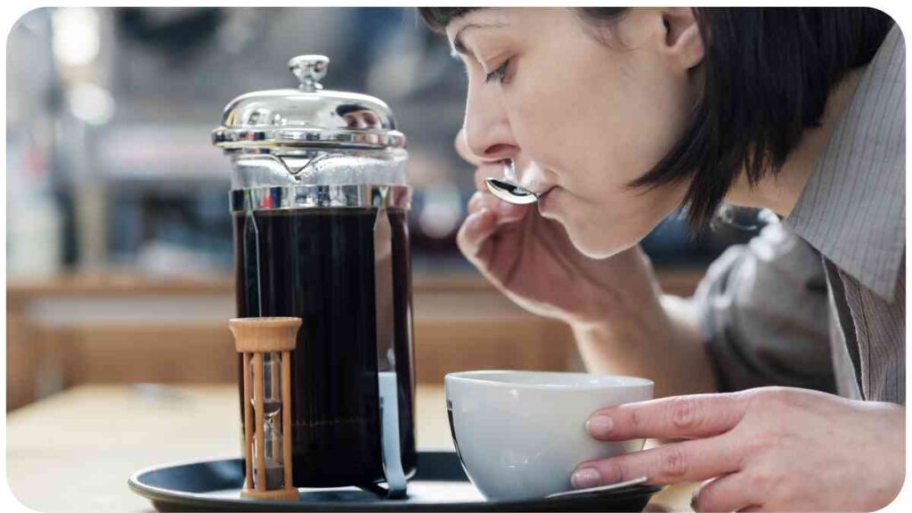 a person drinking a cup of coffee in front of a french press
